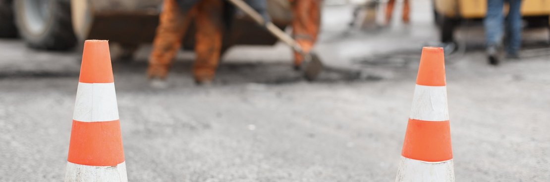 Straßenarbeiter bei der Arbeit. Zwei Pylonen sichern die Straße.